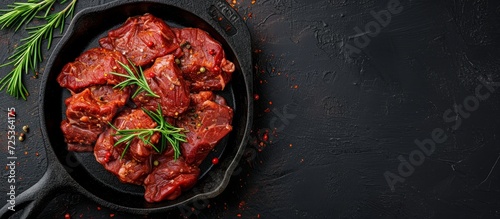 Top view of a cast iron skillet with cayenne pepper-spiced raw meat on a black background.