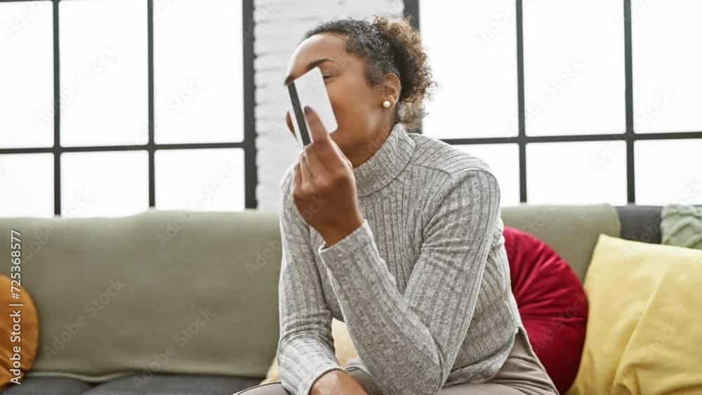 Smiling woman holding credit card in cozy living room, with window, sofa, and cushions Smiling woman holding credit card in cozy living room, with window, sofa, and cushions