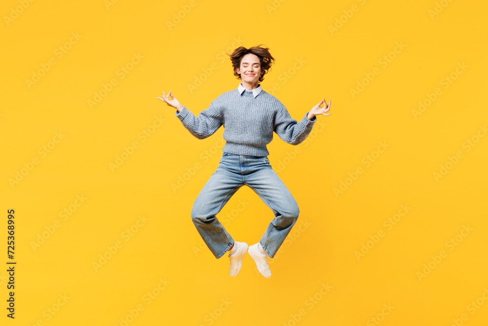 Full body young woman wear grey knitted sweater shirt casual clothes jump high hold spreading hands in yoga om aum gesture relax meditate try to calm down levitate isolated on plain yellow background