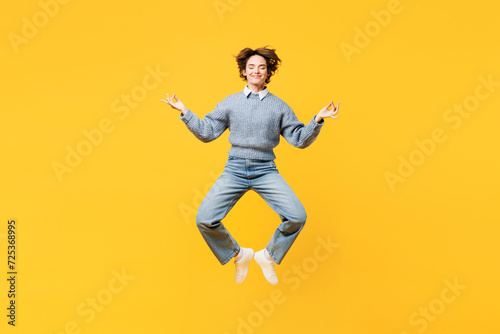 Full body young woman wear grey knitted sweater shirt casual clothes jump high hold spreading hands in yoga om aum gesture relax meditate try to calm down levitate isolated on plain yellow background © ViDi Studio