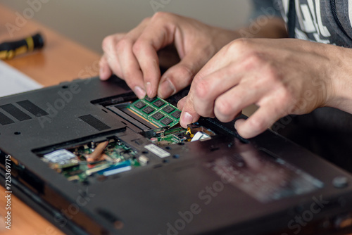 Closeup of male technician installing ram memory module in laptop motherboard, Precision cleaning: Expert repairs and cleans a laptop for optimal performance