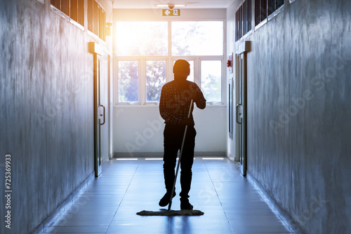 Fotografie Janitor man mopping floor in hallway office building or walkway after school and classroom silhouette work job with sun light background
