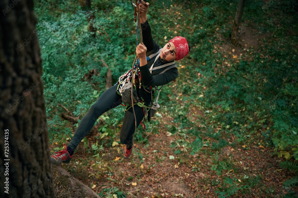 Naklejka premium Focused on the climbing up. Woman is in the forest, using the safety equipment