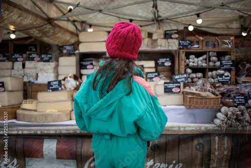 A girl wearing a snow suit observing a stall with local specialties at the marketplace in Lanslevillard, a small, picturesque town in the French Alps