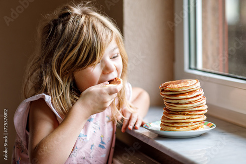 Little happy preschool girl with a large stack of pancakes for breakfast. Positive child eating healthy homemade food in the morning.