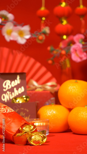 Chinese Lunar New Year background. ancient Chinese gold bar in silk bag, red gift box with text best wishes, orange, paper fan, plum blossom branch, candle and ornament hanging at background © asiandelight