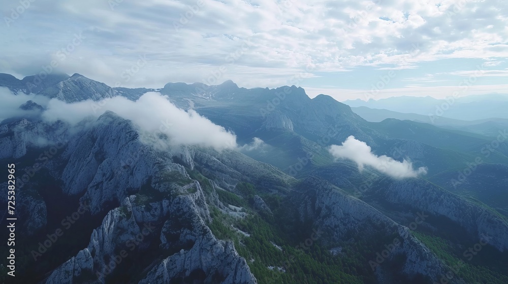 An aerial view, shot from a drone, shows a mountain range with clouds in the sky.
