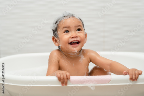happy infant baby take a bath and playing with foam bubbles in bathtub