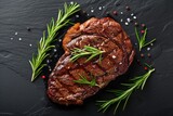 Roasted beef steak on dark stone background with rosemary herbs. Top view