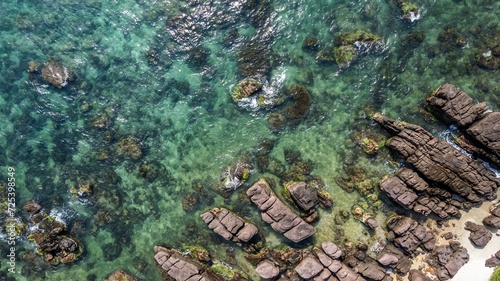 Aerial view of a clear turquoise sea washing over a rocky shoreline, showcasing natural textures and coastal beauty