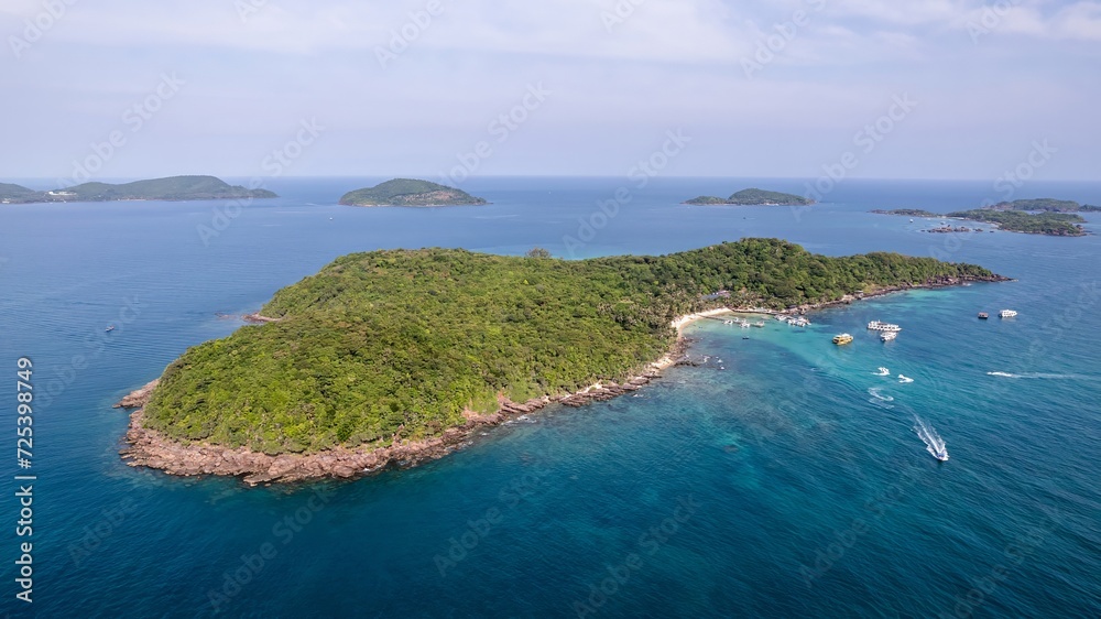 Aerial view of a tropical island with dense forestation surrounded by clear blue water and boats near the coastline, illustrating a vacation or travel concept