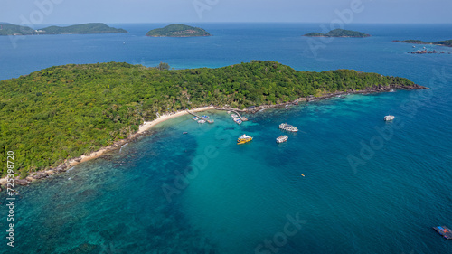 Aerial view of a tropical island with clear blue waters, lush greenery, and boats anchored near the beach, ideal for summer vacation concepts