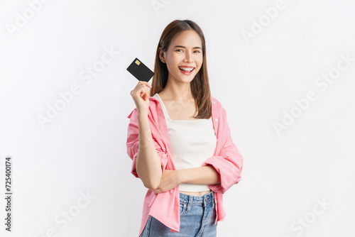 Cheerful beautiful Asian woman wearing pink shirt and holding mockup credit card isolated on white background.