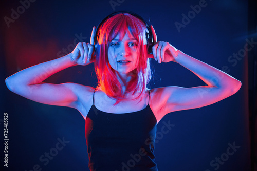 Conception of music, listening in headphones. Woman with white hair is in studio with neon colors