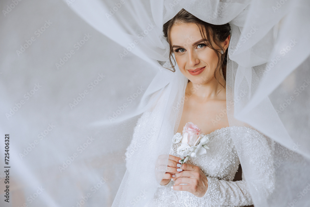 Beautiful young bride holding veil in white wedding dress, portrait of brunette bride in hotel room, morning before wedding.