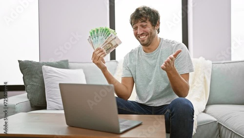 Excited young man, laptop aglow, joyfully celebrates business win at home, waving russian rubles with a winner's smile in a triumphant achievement photo