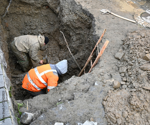 Plumbers repairing a sewer in a dug hole
