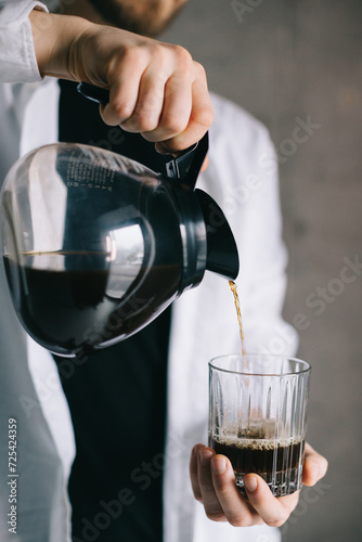 Handsome barista pouring freshly brewed drip coffee in a glass mug. Preparing coffee alternative method.