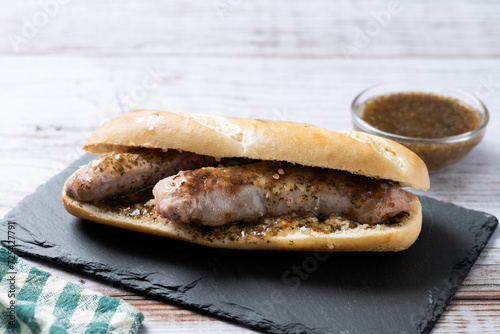 Traditional choripan, Argentina sandwich with chorizo and chimichurri sauce on wooden table