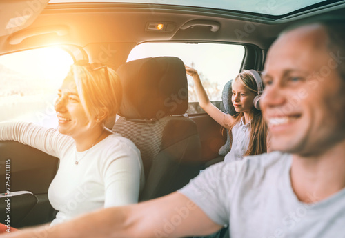 Happy young couple with daughter inside the modern car with panoramic roof during auto trop. They are smiling, laughing during road trip. Family values, traveling concepts.. photo