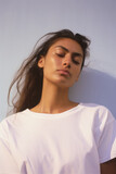 Young adult pretty Indian woman beauty model wearing white t-shirt posing with eyes closed on color background. Face flawless fresh skin hair care cosmetic treatment makeup products skincare ads .