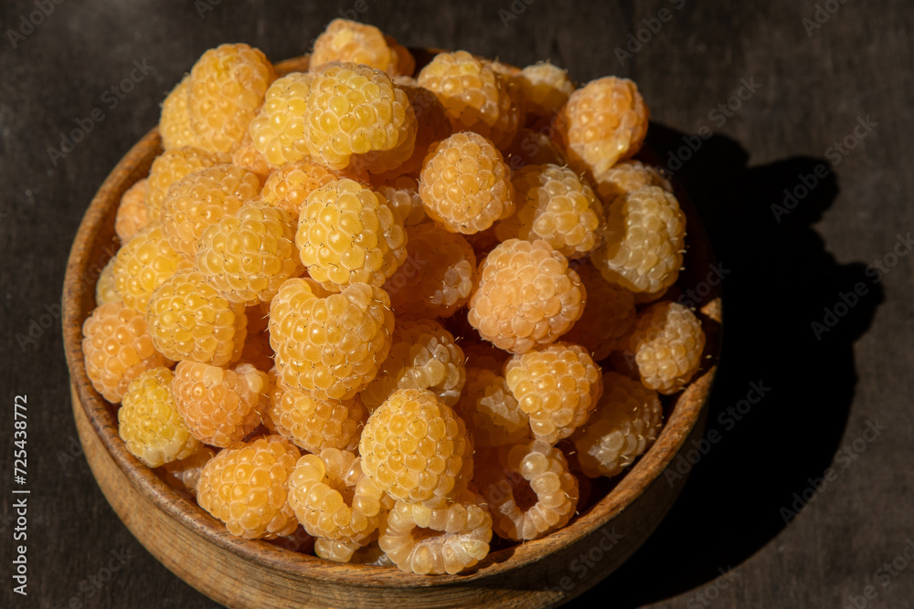 Yellow raspberries in a wooden bowl on the table. Summer berries background. Vitamin food, berry harvest. Healthy nutrition.