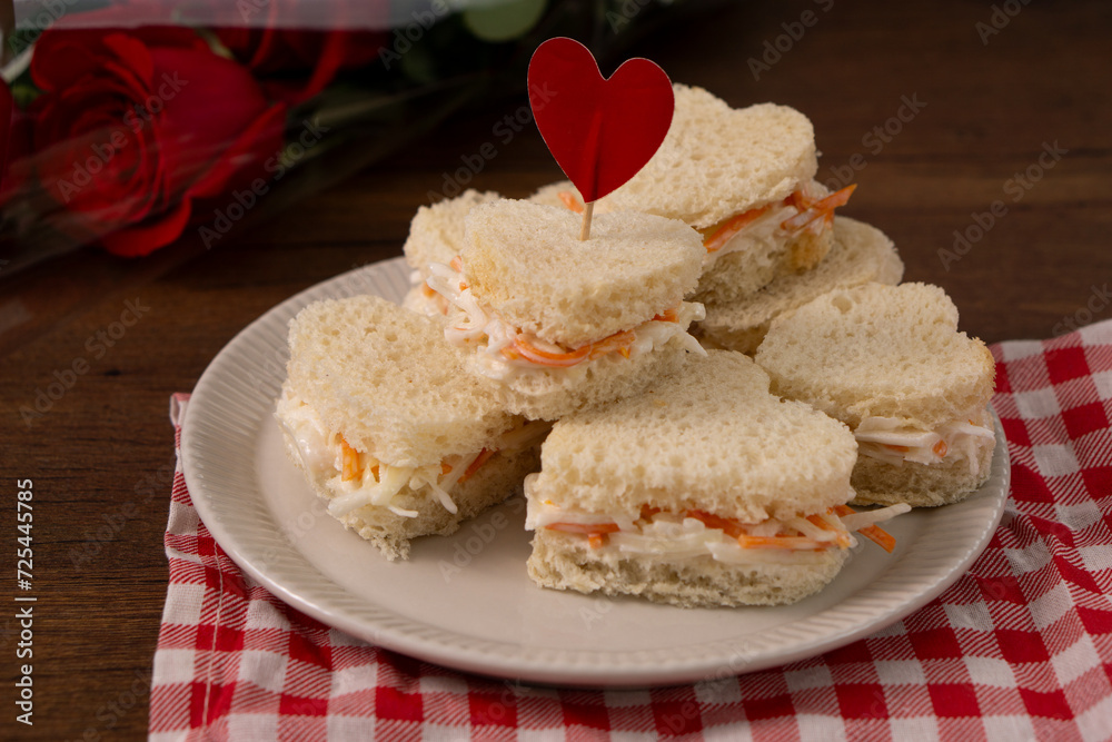 Heart shaped sandwiches made of salad sitting on a white dish on a red and white checkered cloth. There is a roses bouquet on the background. saint Valentines' food. Horizontal image Heart shaped sandwiches made of salad sitting on a white dish on a red and white checkered cloth. There is a roses bouquet on the background. saint Valentines' food. Horizontal image