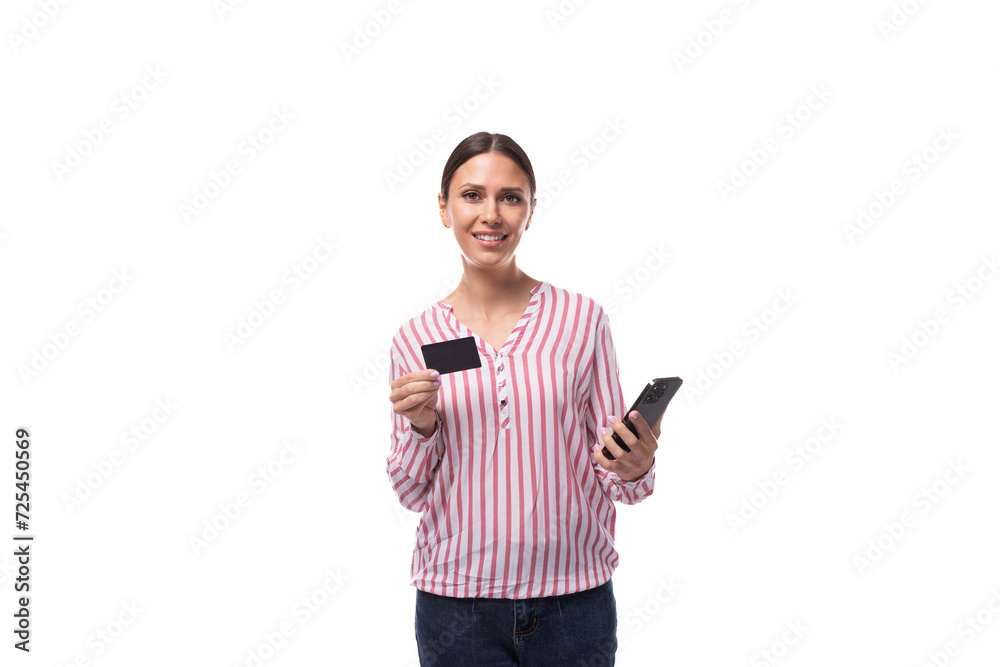 young successful positive brunette leader woman with a ponytail hairstyle dressed in a striped pink and white shirt holds a credit card with a mockup and a smartphone for payment young successful positive brunette leader woman with a ponytail hairstyle dressed in a striped pink and white shirt holds a credit card with a mockup and a smartphone for payment