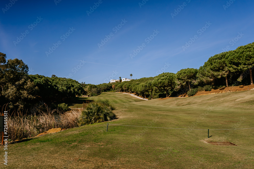 Sotogrante, Spain - January 25, 2024 - A scenic view of a golf course with a clear sky, greenery, and a villa in the distance.
