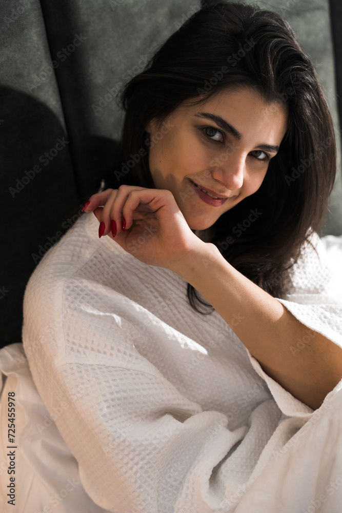 Fototapeta premium A nice woman wakes up in a hotel room and enjoys the view from the window in winter. Coffee in bed. Hotel holiday concept
