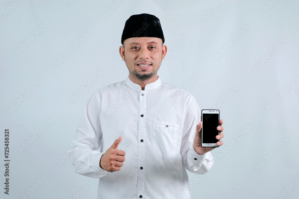 Happy asian muslim man holding and pointing on phone cellular over white background. Ramadan concept