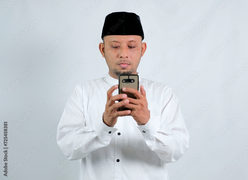 Happy asian muslim man holding and pointing on phone cellular over white background. Ramadan concept Happy asian muslim man holding and pointing on phone cellular over white background. Ramadan concept