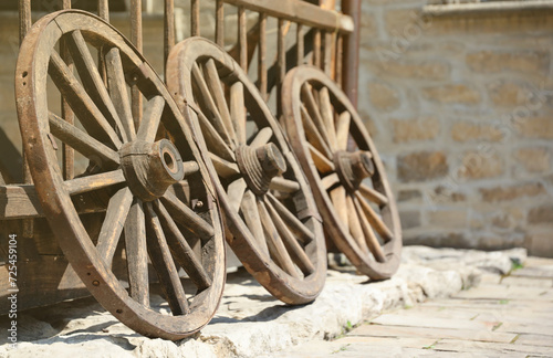 Three old wooden wheels for horse carts leaning against a wooden wall in perspective photo