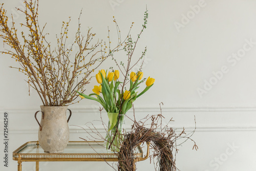 Close-up of a bunch of yellow tulips in a vase on a table with a rustic wreath and jug with branches photo