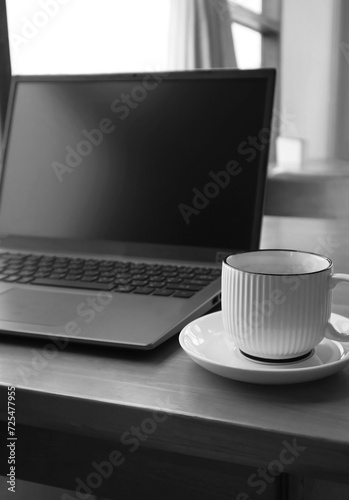 Monochrome Image of a Cup of Coffee with an Opened Blank Screen Laptop photo