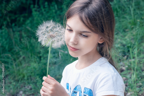 Closeup portrait of a beautiful little girl on the background of a green field with a big dandelion in her hand