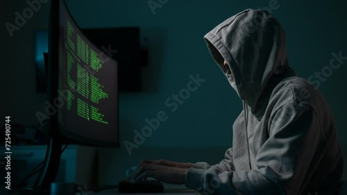 Professional male hacker typing text on keyboard looking to computer ultrawide curved monitor with green text code. Computer hacker typing code on keyboard late night working bypassing cyber security. photo