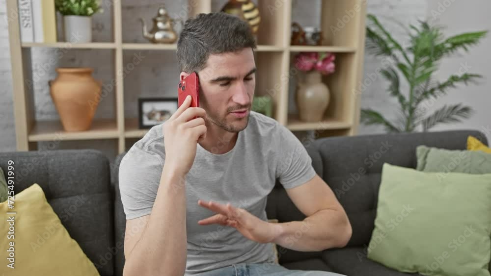 Handsome young man talking on a red smartphone in a modern living room, showing emotions of confusion, frustration, and curiosity. Handsome young man talking on a red smartphone in a modern living room, showing emotions of confusion, frustration, and curiosity.