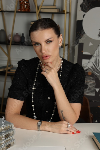 Serious business woman officially dressed in black twid dress. Beautiful  Office manager work at the table with books,  cup of tea. Lady portrait. Bookshelf photo