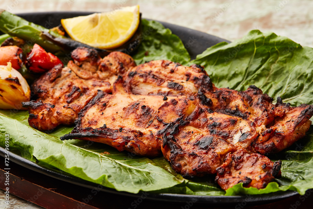 Grilled Chicken with lemon slice and tomato served in dish isolated on table top view of arabic food