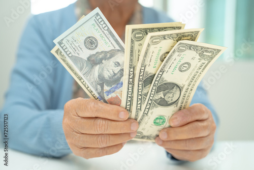 Asian senior woman holding and counting US dollar banknotes money in purse. Poverty, saving problem in retirement.