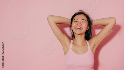 Asian woman in white t-shirt put her hands behind her head in against light pink studio background