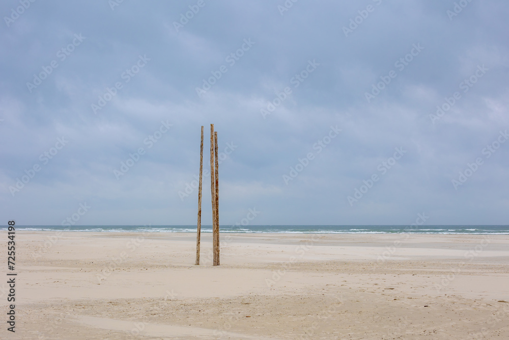 Wide and long sand beach under white grey cloudy sky, Wooden pole along the seashore of the Dutch Wadden Sea island Terschelling, A municipality and an island in the northern, Friesland, Netherlands. Wide and long sand beach under white grey cloudy sky, Wooden pole along the seashore of the Dutch Wadden Sea island Terschelling, A municipality and an island in the northern, Friesland, Netherlands.