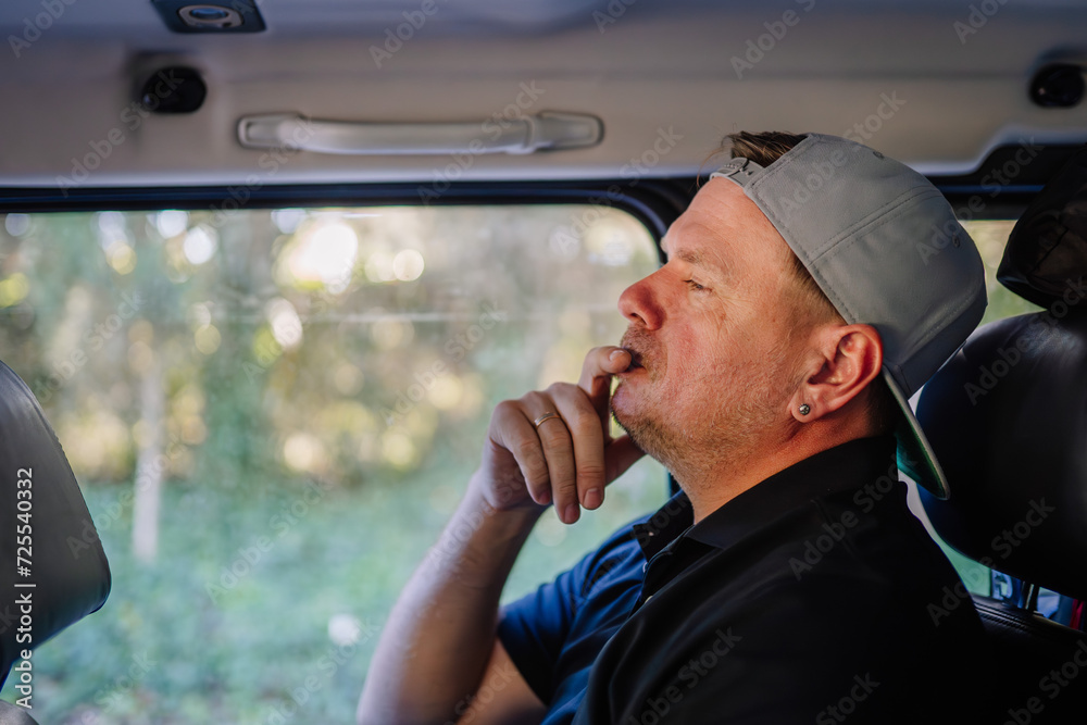 Sotogrante, Spain - January 25, 2024 - a man sitting inside a vehicle, looking thoughtful, with trees visible through the window. Sotogrante, Spain - January 25, 2024 - a man sitting inside a vehicle, looking thoughtful, with trees visible through the window.