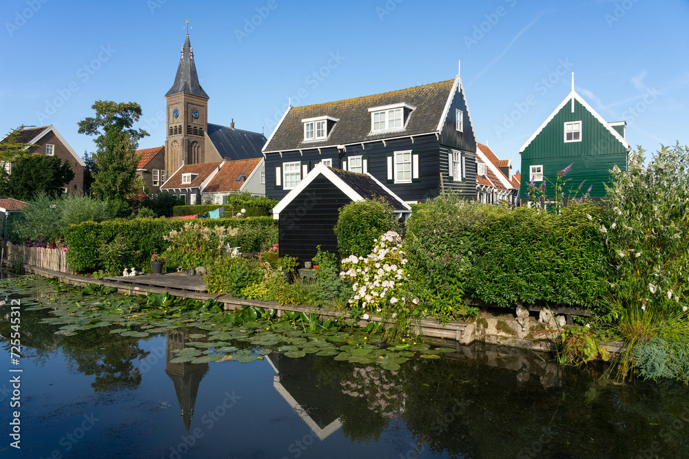 Obraz premium View of the beautiful and typical fishing village of Marken in Netherlands at sunset reflected on a canal.