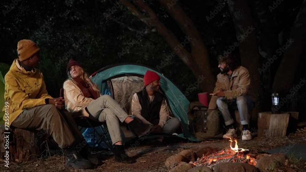 Young multiracial group of friends camping outdoors and sitting around campfire on the forest at night, speaking and enjoying their trip adventure. Young multiracial group of friends camping outdoors and sitting around campfire on the forest at night, speaking and enjoying their trip adventure.