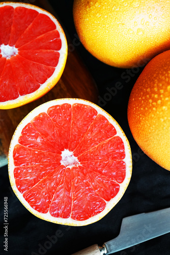 Sliced       and whole grapefruit on a wooden board next to a knife on a dark background