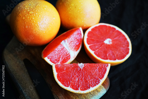 Sliced       and whole grapefruit on a wooden board next to a knife on a dark background