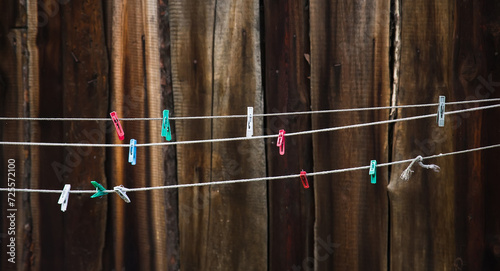 Colorful clothespins hanging on washing line or rope against the background of a wooden fence.