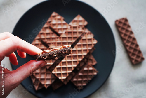 Chocolate wafer in a woman's hand against the background of other chocolate waffles on a black plate